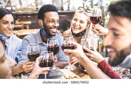 Friends toasting red wine glasses at outdoor restaurant bar with open face mask - New normal lifestyle concept with happy people having fun together on warm filter - Focus on left guy - Powered by Shutterstock