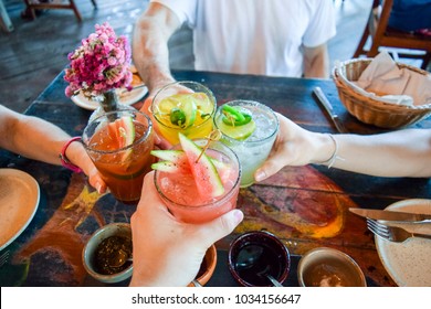 Friends toasting, saying cheers holding tropical blended fruit drinks - Shutterstock ID 1034156647