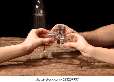 Friends toasting with shot glasses above an old wooden table black background - Powered by Shutterstock