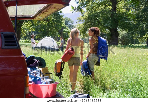 Friends unload camping equipment and tent\
from car boot in\
countryside