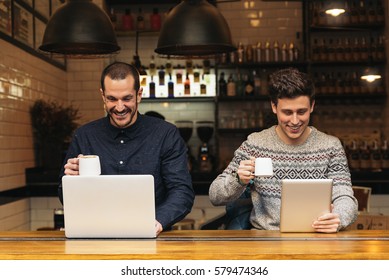 Friends Using Mobile And Laptop In A Coffee Shop.