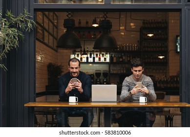 Friends Using Mobile And Laptop In A Coffee Shop.