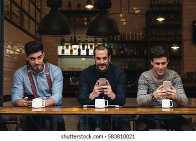 Friends Using Mobile And Laptop In A Coffee Shop.