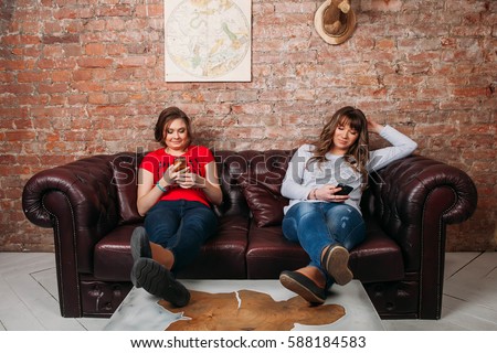 Friends using phone while sitind on sofa at living room Technology, education and friendship concept