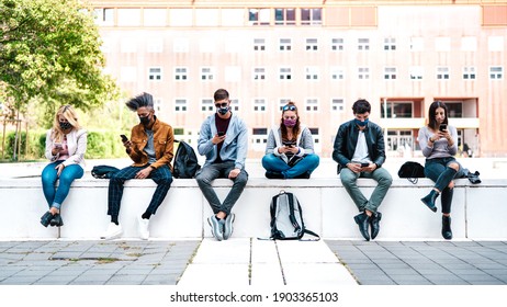 Friends Using Smart Phone Covered By Mask On Covid Third Wave - Worried Guys And Girls Watching Video News On Mobile Smartphone - College Students Sitting At University Campus - Focus In Central Faces