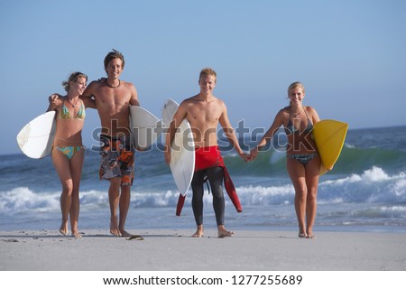 Friends walking in surf on summer beach vacation with surfboards holding hands