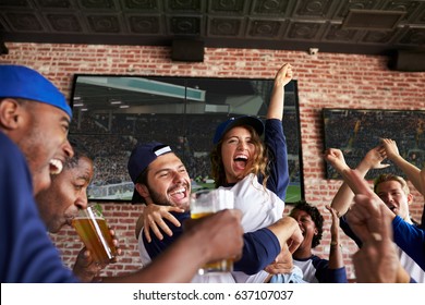 Friends Watching Game In Sports Bar On Screens Celebrating