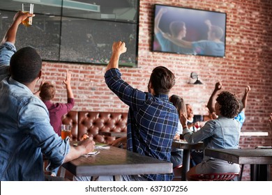 Friends Watching Game In Sports Bar On Screens Celebrating