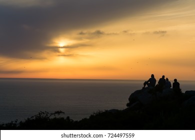 Friends Watching Sunrise On A Rock On The Spanish Coast, While Watching The Horizon