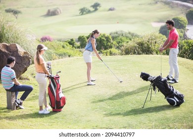 Friends Watching Woman Teeing Off On Golf Course