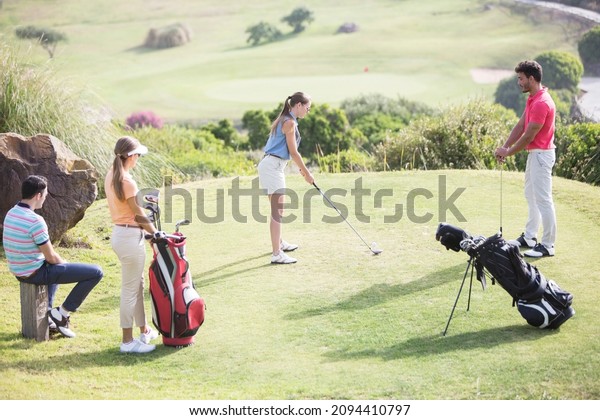 Friends watching\
woman teeing off on golf\
course