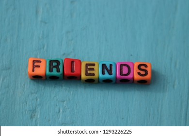 Friends word spelled out in primary colors colorful abc alphabet beads blocks on blue wood background.