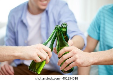 Friendship, Alcohol, People, Celebration And Holidays Concept - Close Up Of Male Friends Drinking And Clinking Beer Bottles At Home