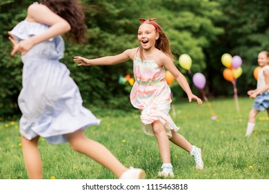 friendship, childhood, leisure and people concept - group of happy girls or friends playing tag game at birthday party in summer park