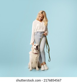 Friendship concept. Happy woman posing with her happy labrador dog on a leash, looking at her pet standing isolated on blue studio background wall, full body length - Powered by Shutterstock