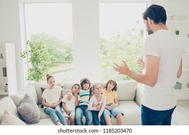 Friendship concept. Now I will tell you the most interesting story! Lovely, beautiful kids sit on couch in modern light interior while the father gesticulates with his hands and tells news, ideas