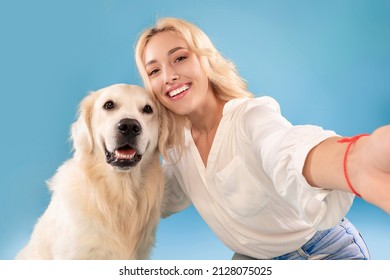 Friendship Concept. Portrait of excited beautiful caucasian blonde woman taking selfie with her happy dog, posing looking at camera, isolated on blue studio background wall, closeup