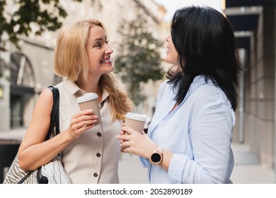 Friendship concept. Two caucasian mature women best friends girlfriends sisters communicating talking spending time together while walking on the streets and drinking hot beverage from paper cup - Powered by Shutterstock