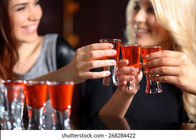Friendship forever. Selective focus on three shots with red beverage and smiling girls in blurry holding glasses