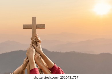 Friendship hands praying and holding Christian cross for worshipping God on mountain at sunrise background. Christian, Christianity, Religion copy space background. Easter Sunday concept: