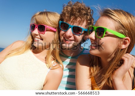 Friendship happiness summer holidays concept. Group of friends boy two girls in colorful sunglasses having fun outdoor against sky,  joy playful mood.