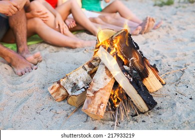 Friendship, Happiness, Summer Vacation, Holidays And People Concept - Close Up Of Friends Sitting Near Fire On Beach