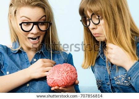 Friendship, human relations concept. Two crazy women friends or sisters wearing jeans shirts and eyeglasses on stick, thinking about solving problem holding fake brain