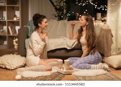 friendship, hygge and pajama party concept - happy female friends or teenage girls eating waffles with cacao at home - Powered by Shutterstock