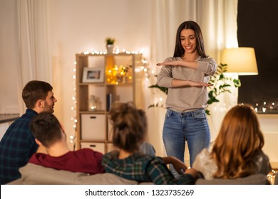 Friendship, Leisure And Entertainment Concept - Happy Friends Playing Charades Game At Home In Evening