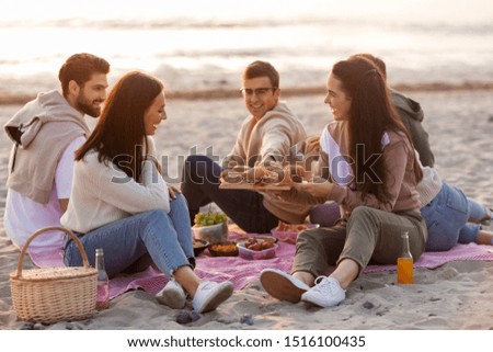 friendship, leisure and fast food concept - group of happy friends eating sandwiches or burgers at picnic on beach in summer