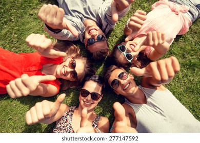 friendship, leisure, summer, gesture and people concept - group of smiling friends lying on grass in circle and showing thumbs up outdoors - Powered by Shutterstock