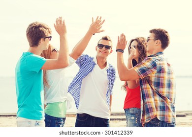 Friendship, Leisure, Summer, Gesture And People Concept - Group Of Smiling Friends Making High Five Outdoors