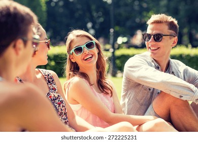 Friendship, Leisure, Summer And People Concept - Group Of Smiling Friends Outdoors Sitting On Grass In Park