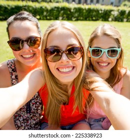 Friendship, Leisure, Summer, Technology And People Concept - Group Of Smiling Teen Girls Taking Selfie With Smartphone Camera Or Tablet Pc In Park