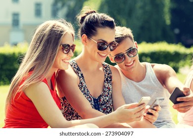 friendship, leisure, summer, technology and people concept - group of smiling friends with smartphone sitting on grass in park - Powered by Shutterstock