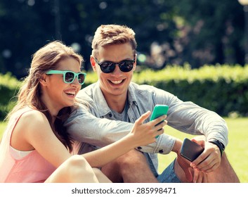 friendship, leisure, summer, technology and people concept - group of smiling friends with smartphone sitting on grass in park - Powered by Shutterstock