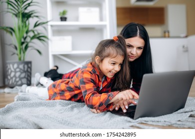 Friendship Of Mom And Her Cute Little Daughter. They Wallow At Home On The Floor In Casual Clothes And Shopping Online Together Using A Laptop. They Buy New Toys For Pretty Little Girl