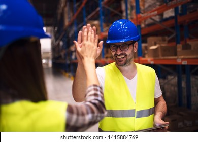 Friendship on job. Good relationship between two coworkers. Warehouse worker giving high five to his friend colleague. Workers hands touching and clapping for successfully done job in warehouse.