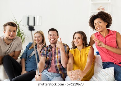 Friendship, And People Concept - Group Of Happy Friends Taking Picture With Smartphone And Selfie Stick At Home