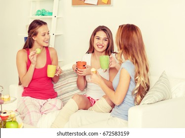 Friendship, People, Pajama Party And Communication Concept - Happy Friends Or Teenage Girls Drinking Tea And Eating Sweets At Home