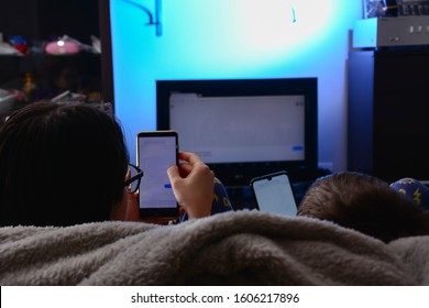 friendship, people, technology and entertainment concept - Back view close up of a woman and 8 year old boy with hands using a smart phones with blank screen lying on a couch at home with tv - Powered by Shutterstock