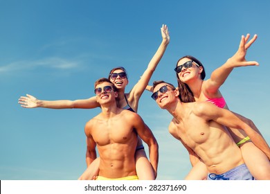 Friendship, Sea, Summer Vacation, Holidays And People Concept - Group Of Smiling Friends Wearing Swimwear And Sunglasses Having Fun On Beach