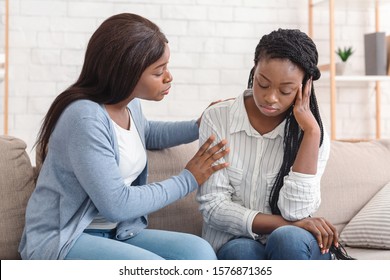 Friendship And Support. Compassionate Black Girl Comforting Her Upset Friend, Soothing Her After Breakup With Boyfriend, Sitting On Sofa At Home.