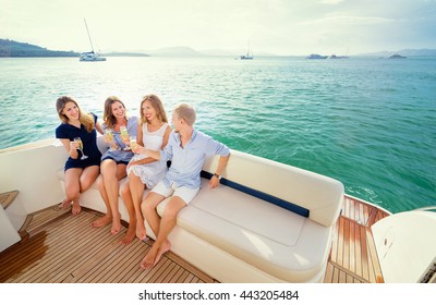 Friendship and vacation. Party on the yacht. Group of laughing young people sitting on the deck drinking champagne sailing the sea.
