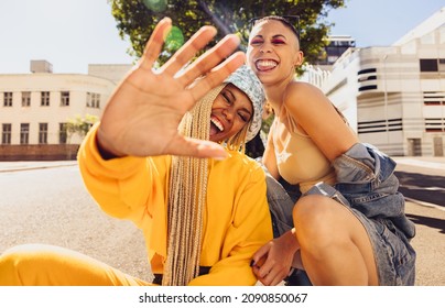 Friendship Vibes Only. Young Trendy Woman Blocking The Camera With Her Hand While Sitting With Her Friend Outdoors. Two Best Friends Smiling Cheerfully And Having Fun In The Summer Sun.