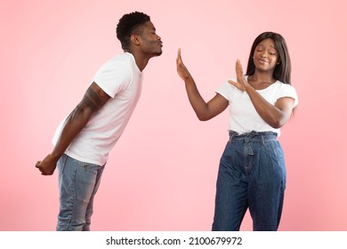Friendzone Concept. Disgusted black woman avoiding unwanted kiss from obsessed man in love who trying to reach her and pulling lips. Angry young lady refusing and showing stop gesture with palms