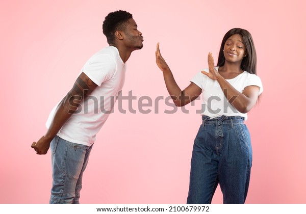 Friendzone Concept. Disgusted black woman avoiding\
unwanted kiss from obsessed man in love who trying to reach her and\
pulling lips. Angry young lady refusing and showing stop gesture\
with palms