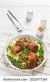 friesd  faggots, english meatballs with creamy mashed potatoes, green peas and rich, thick onion gravy on a white plate, classic british cuisine, vertical view