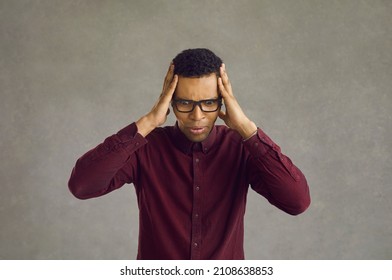 Frightened African-American man nervously grabs his head, realizing his mistake. Worried young man in a cherry shirt and glasses nervous standing on a gray background. Anxiety concept. Banner