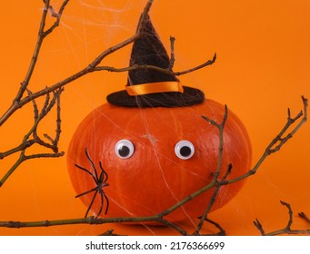 Frightened Animated Pumpkin With Eyes And A Witch Hat And A Branch With Cobwebs On An Orange Background. Halloween Decor